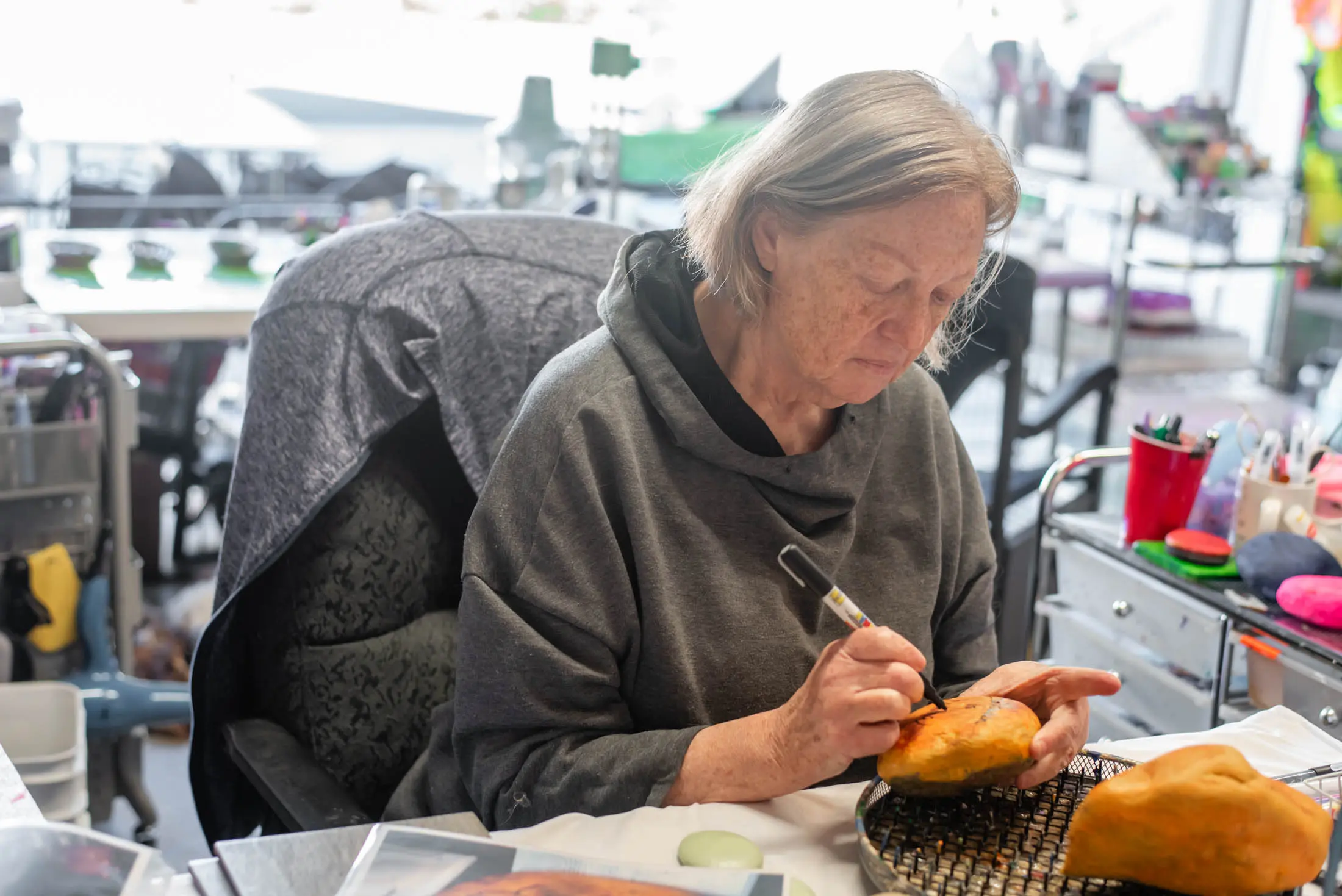 An elderly woman painting a pumpkin with focused attention.